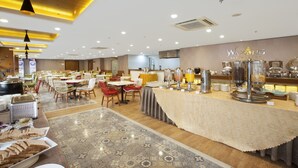 Un comedor amplio con múltiples mesas y sillas, una barra de buffet con diversos alimentos, y un diseño de techo moderno con iluminación empotrada.