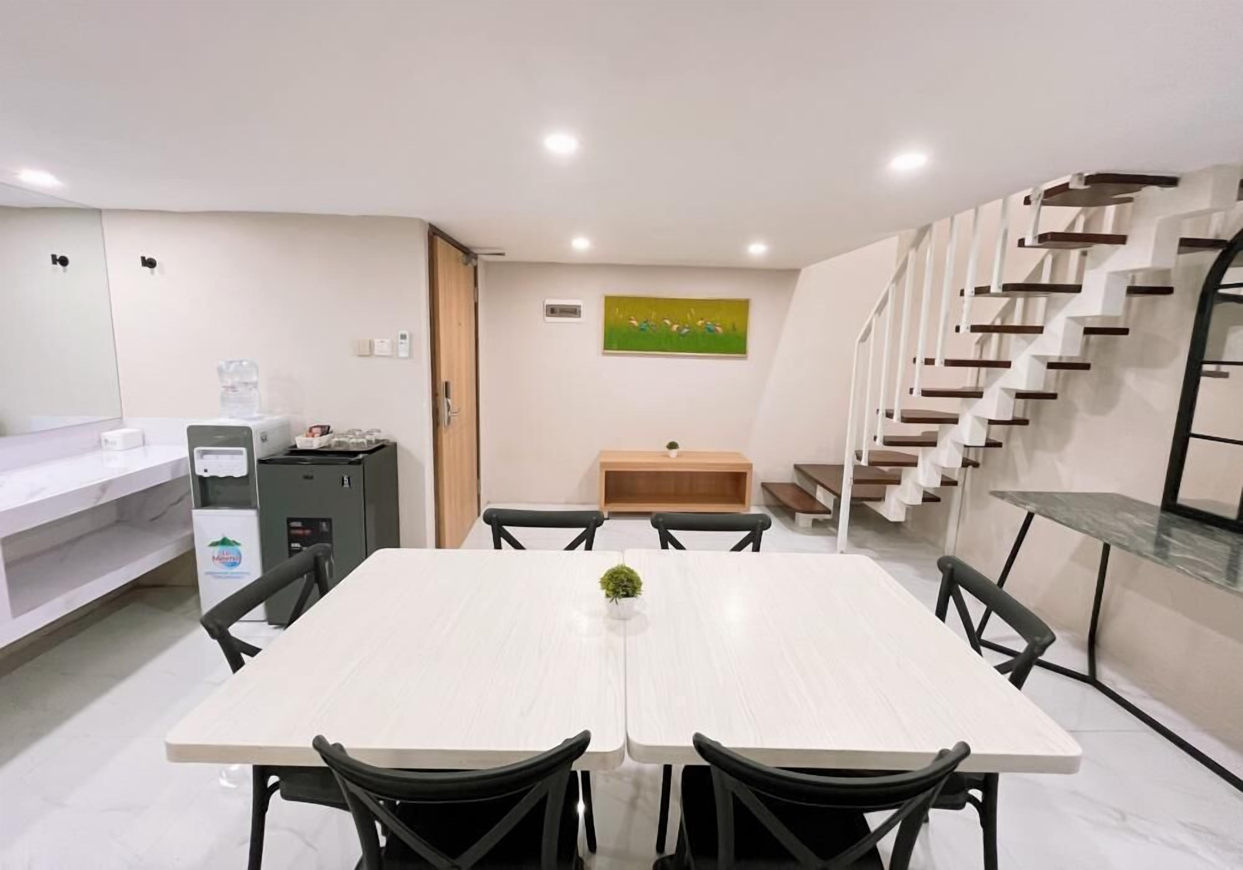 A modern dining area with a white table, black chairs, a small plant, a water dispenser, and a staircase.