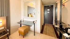 Una habitación de hotel moderna con un escritorio de vidrio, un taburete pequeño, un espejo y una puerta con un letrero que indica un límite de tiempo.