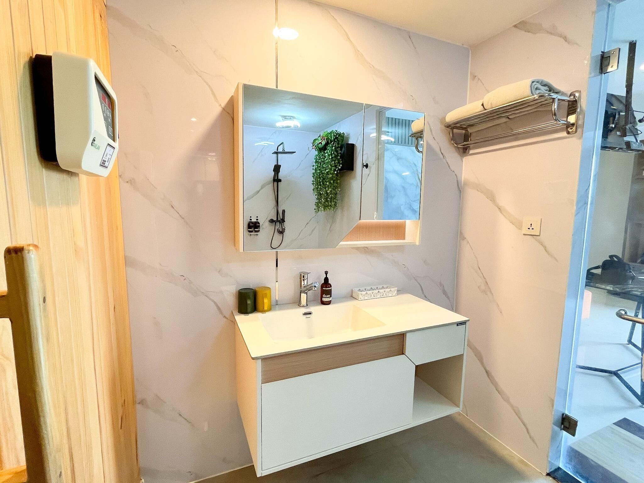 Un baño moderno con pared de mármol, lavamanos integrado, espejo y cabezal de ducha de mano.