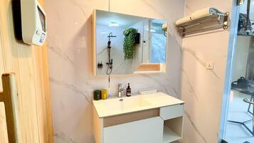 Un baño moderno con pared de mármol, lavamanos integrado, espejo y cabezal de ducha de mano.