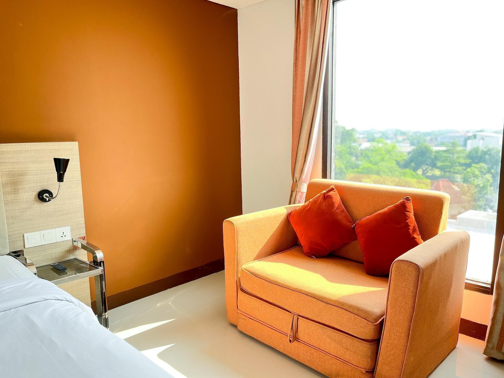 Ein Hotelzimmer mit einer Couch, einem Beistelltisch mit Lampe und Blick ins Grüne.