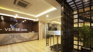 Zona de recepción de un hotel con un mostrador de mármol, una puerta de vidrio y un letrero que dice "VERSE HOTEL".