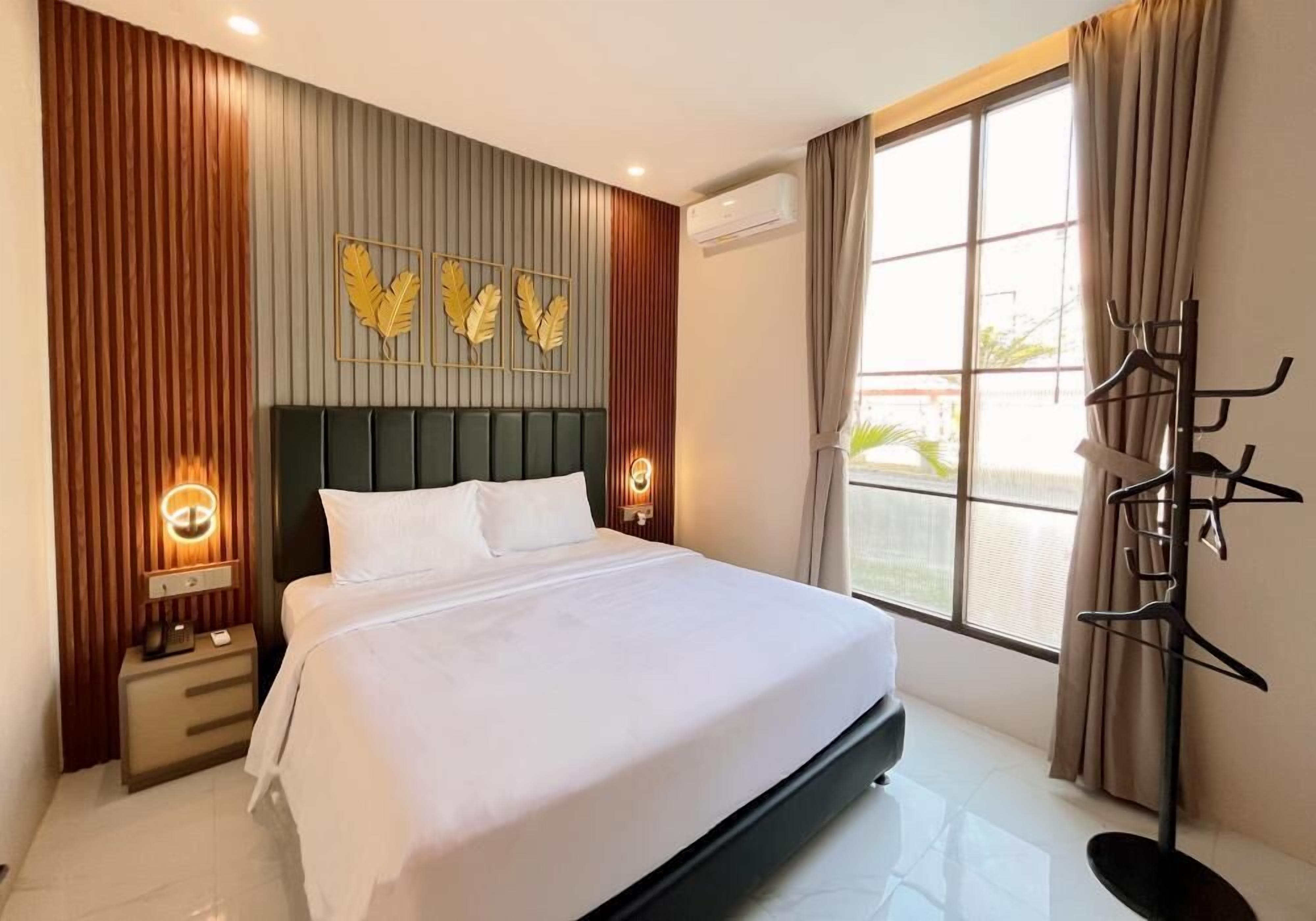 Une chambre d’hôtel avec un lit, des lampes de chevet, un porte-manteau et une fenêtre avec des rideaux.