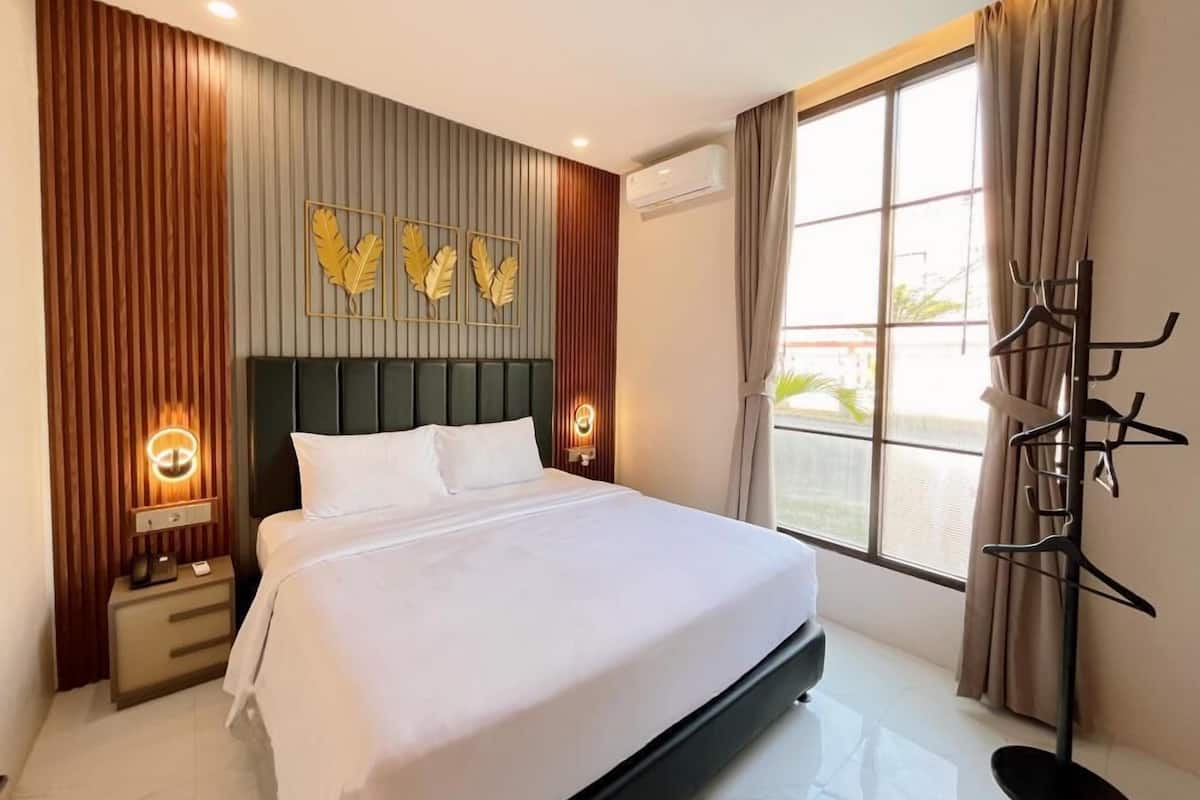 Ein Hotelzimmer mit einem Bett, Nachttischlampen, einem Kleiderständer und einem Fenster mit Vorhängen.