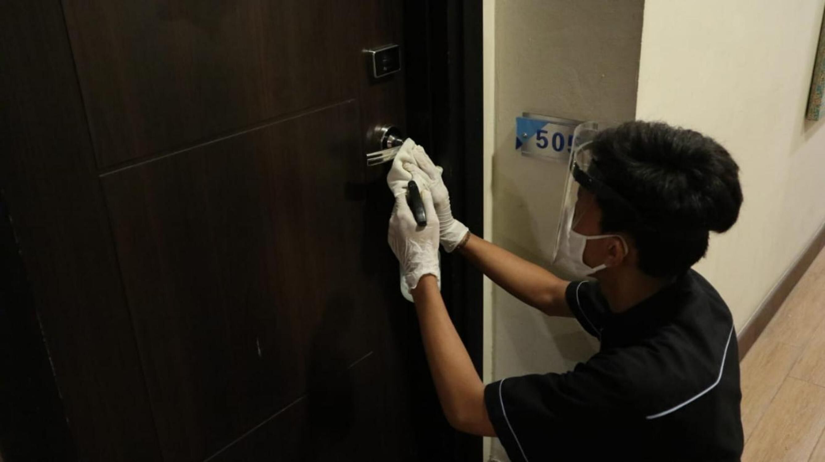 Una persona con guantes y una mascarilla, abriendo una puerta de madera oscura.