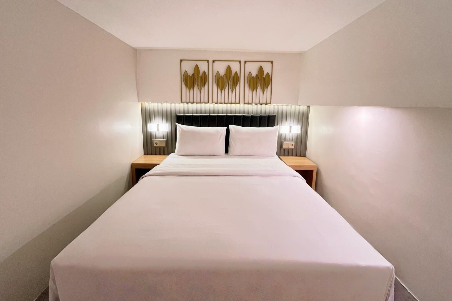 Une chambre d’hôtel avec un grand lit, deux tables de chevet, une tête de lit recouverte d’un tissu foncé et trois appliques murales.