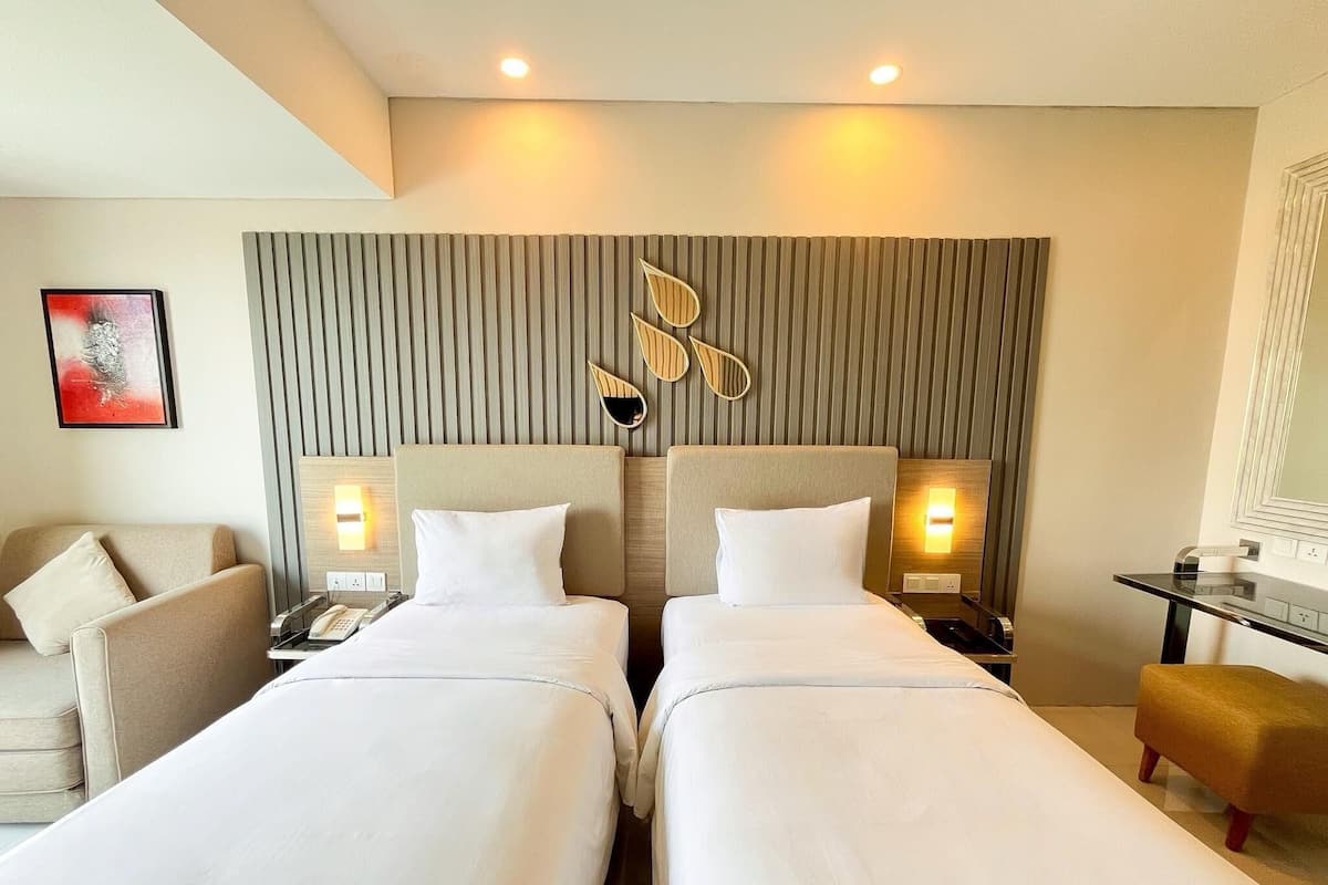 Ein Hotelzimmer mit zwei Betten, einer Sitzecke, einem kleinen Tisch und einer Wandleuchte.