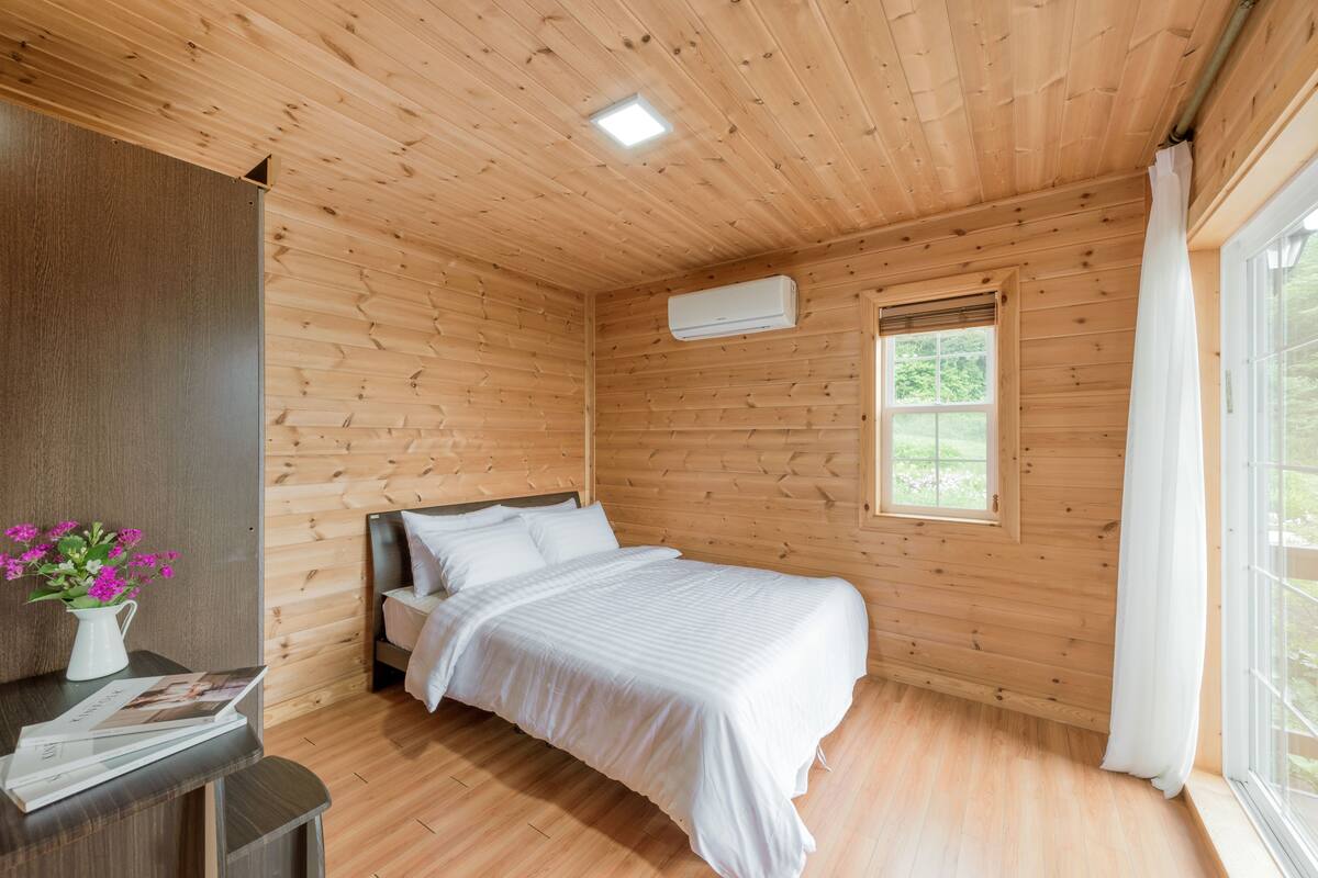 A wooden-paneled room with a bed, a window, and an air conditioning unit.