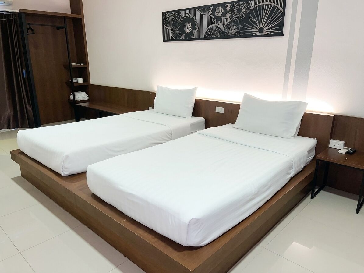 A hotel room with two single beds, a wooden headboard, a nightstand with a phone, and a wall-mounted artwork.