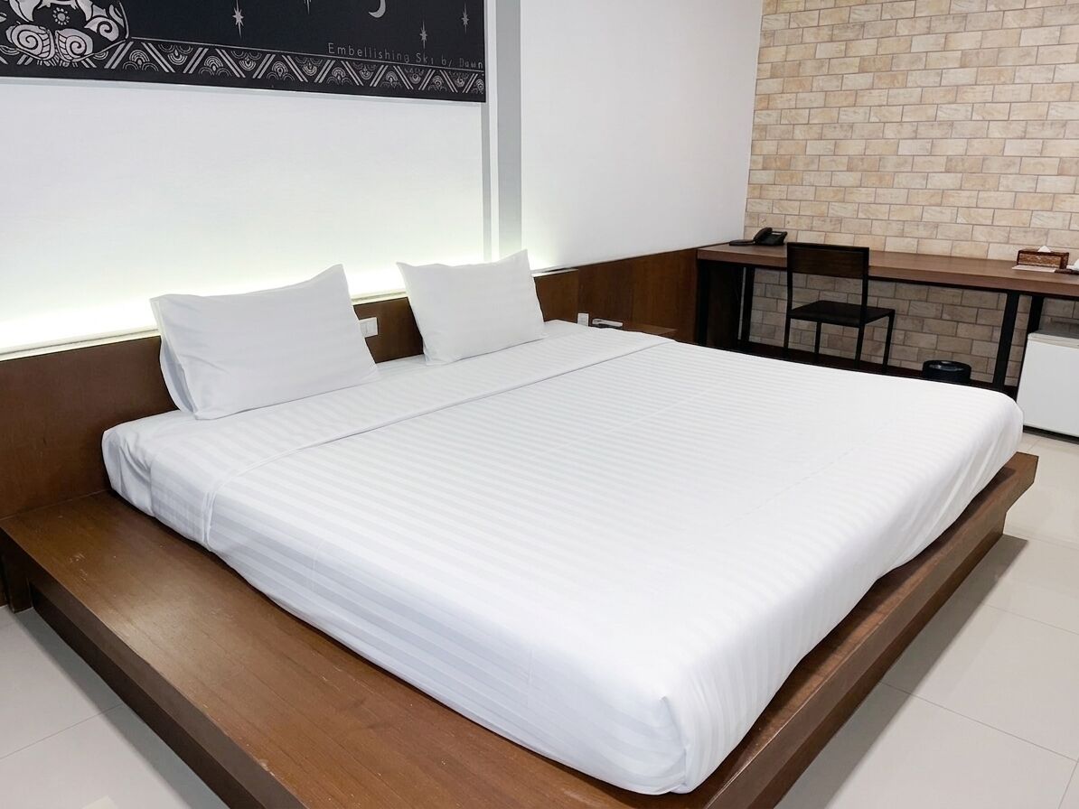 A neatly made bed in a hotel room with a wooden headboard, a desk with a chair, and a brick wall.