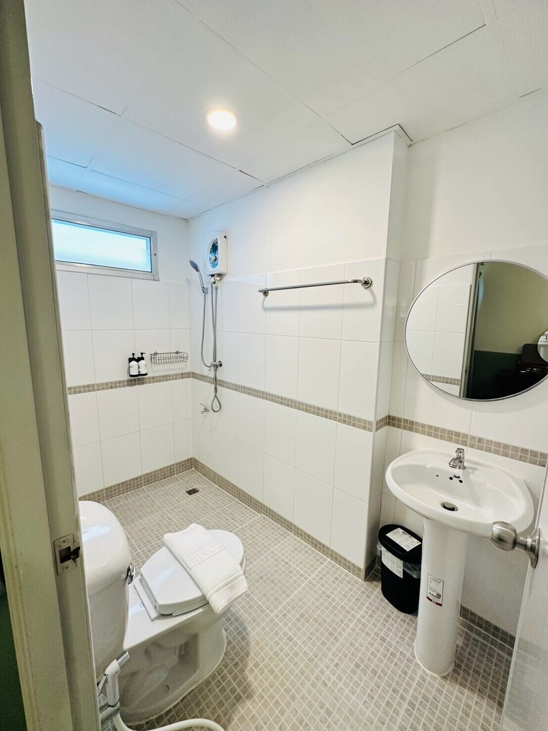 A bathroom with a toilet, sink, shower, and a mirror.