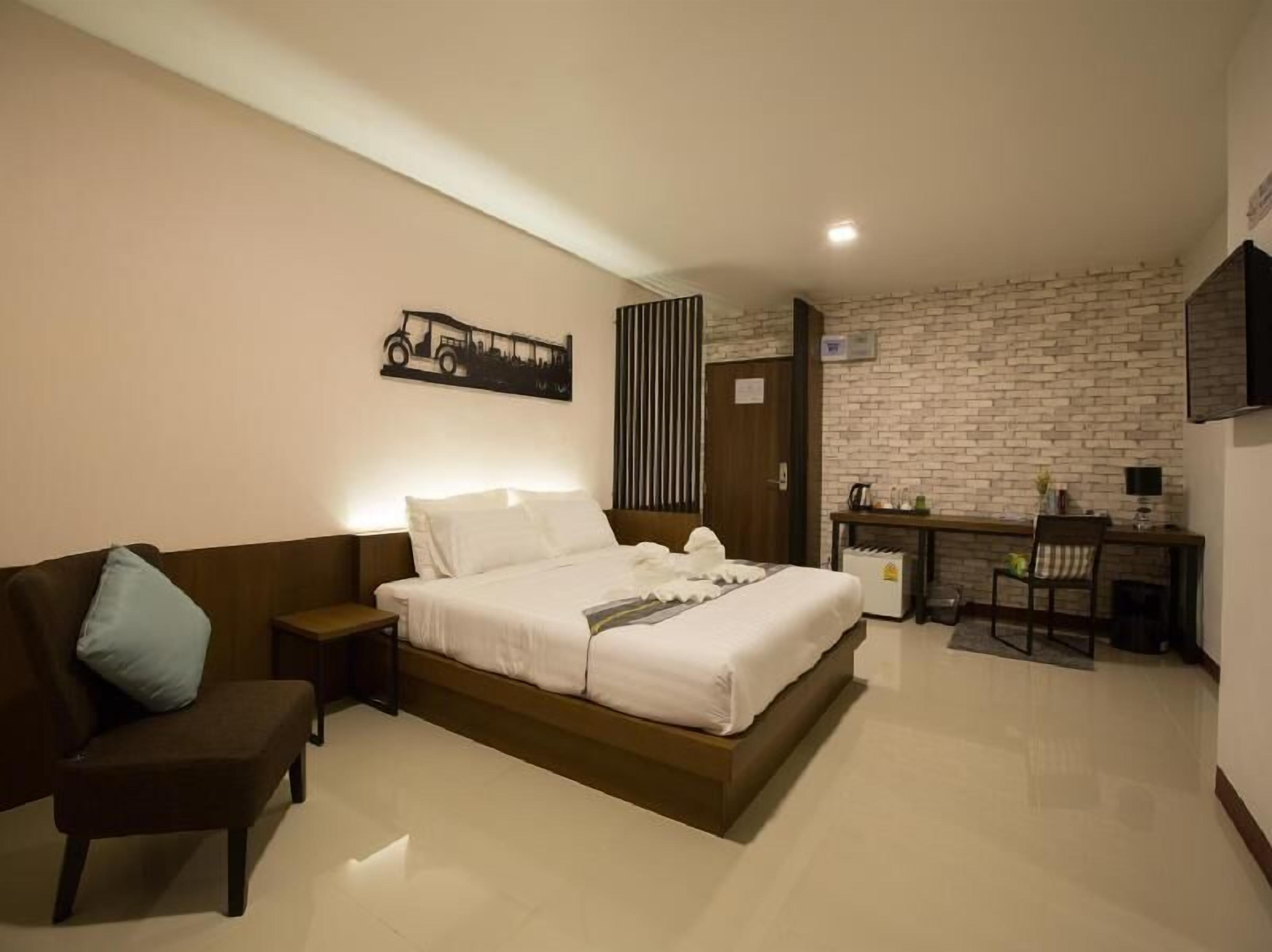 A hotel room with a bed, a desk, a chair, a TV, and a wall-mounted artwork.