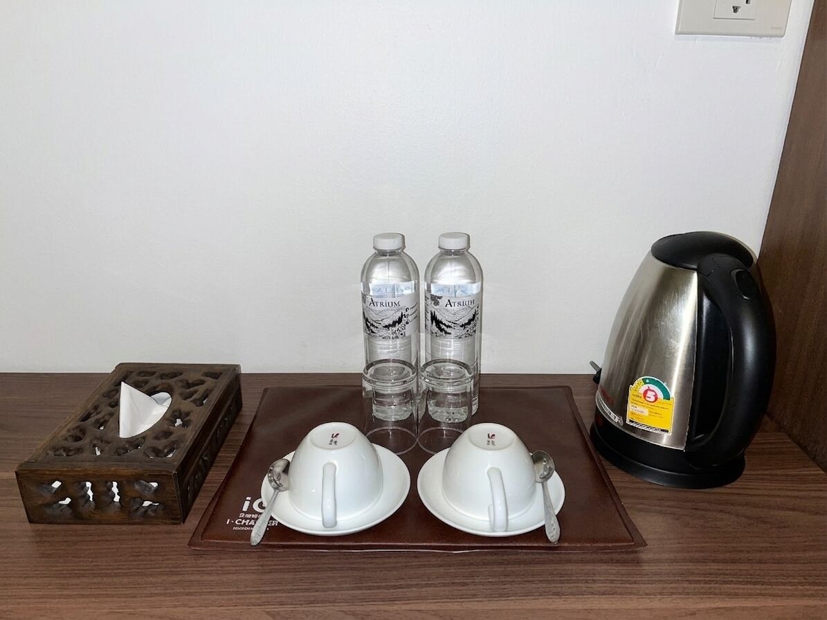 A table with two white teacups, two water bottles, a tissue box, and a black electric kettle.