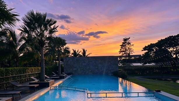 A swimming pool with a stone wall, palm trees, and lounge chairs. - iChapter Hotel Suvarnabhumi (Bang Phli)