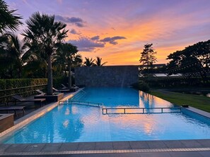 Una piscina con muro de piedra, palmeras y sillas de descanso.