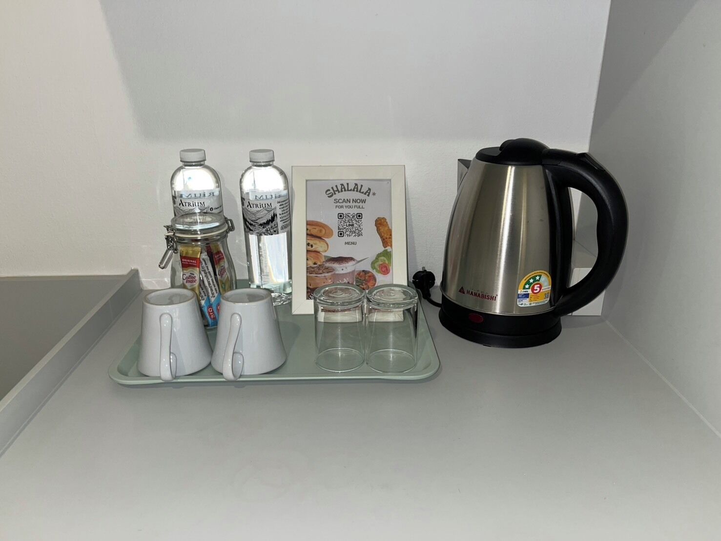 A coffee station with a coffee maker, two thermoses, a tray with cups, and a QR code sign.