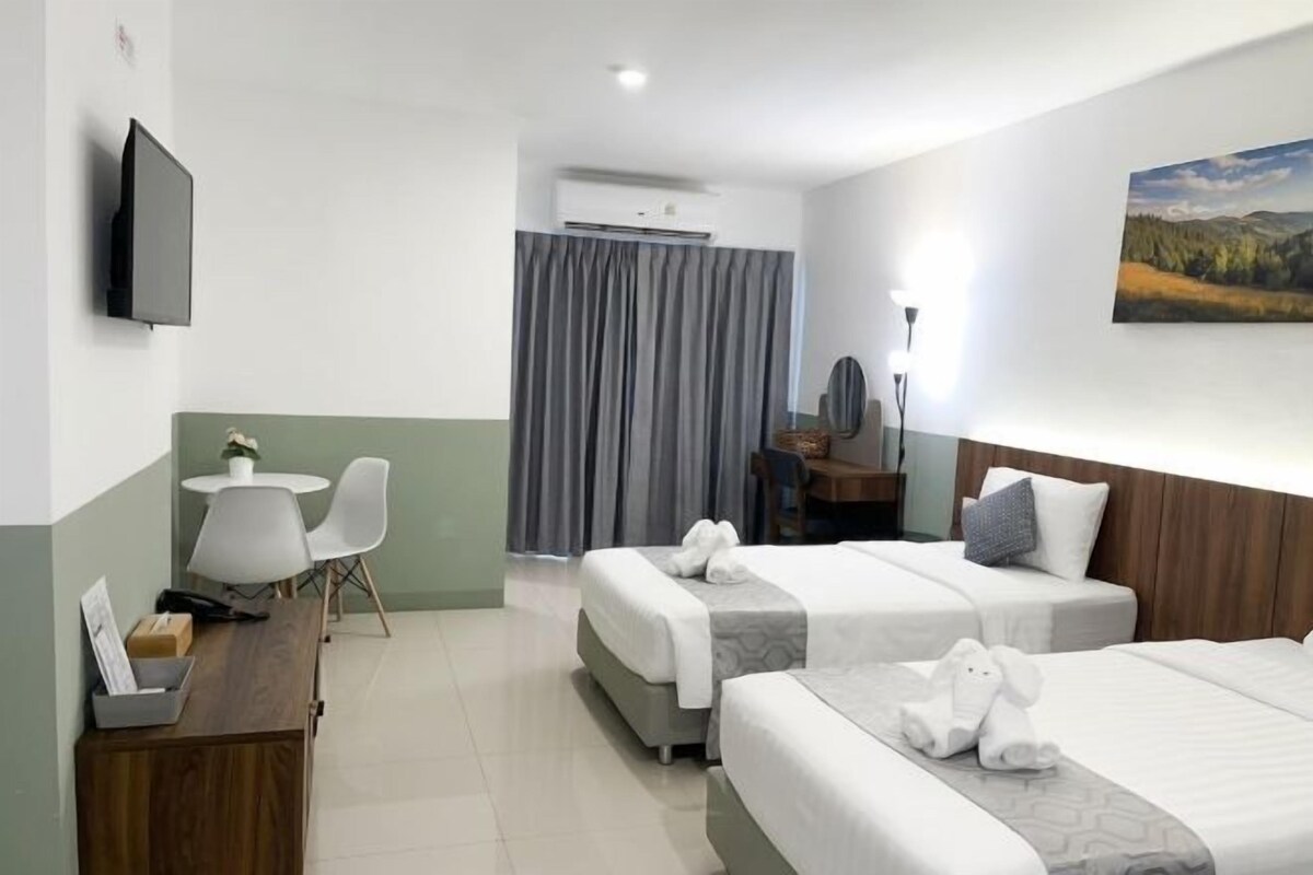 Habitación de hotel con dos camas, un escritorio, una silla, un televisor y una ventana con cortinas.