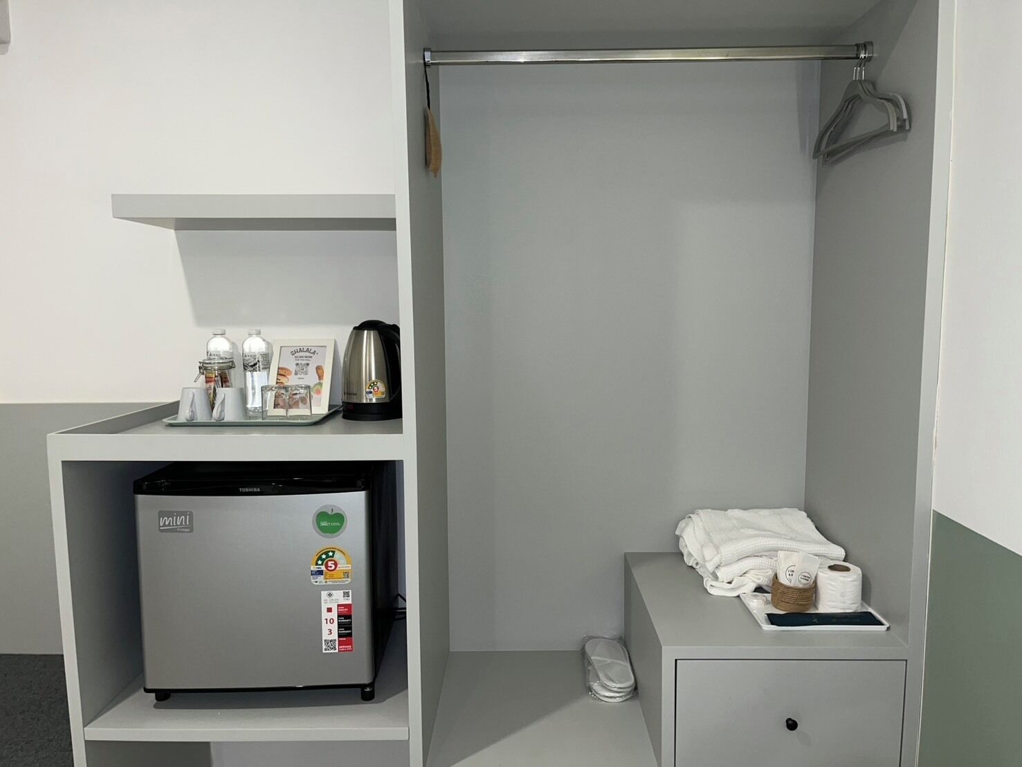 Un baño pequeño con un refrigerador compacto, un perchero y una repisa con artículos de tocador.