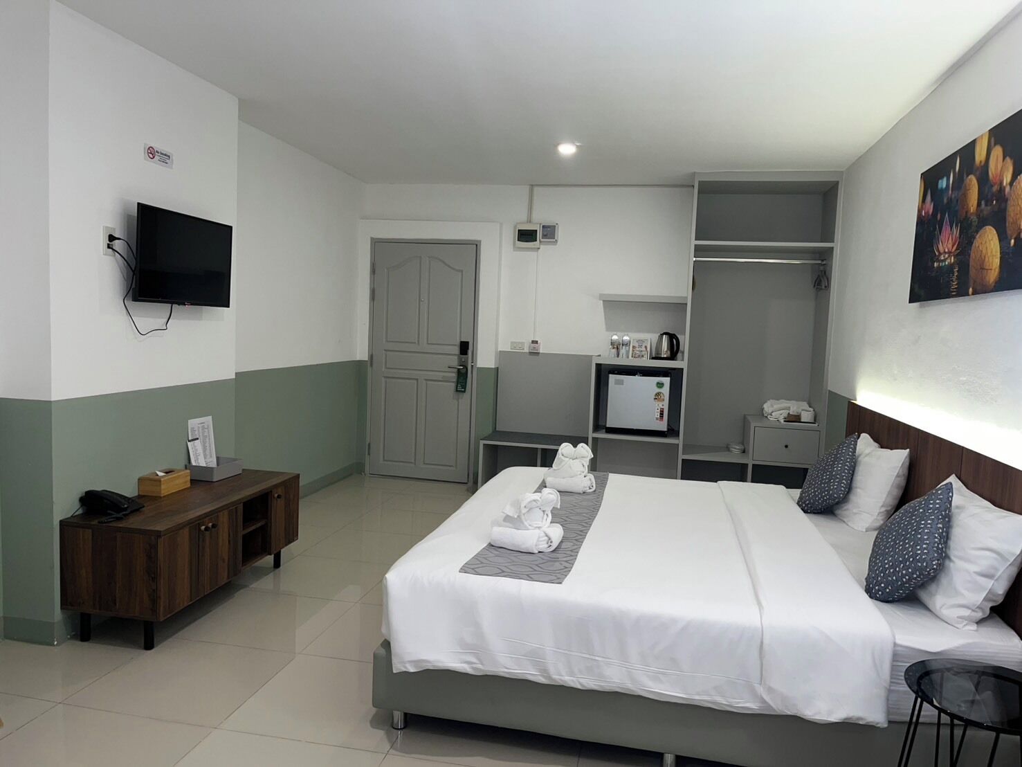 A hotel room with a bed, a television, a desk, a wardrobe, and a painting on the wall.