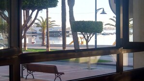 A view through a window of a bench in a parking lot, with trees and a body of water in the background. - Hotel Ribera (San Javier)