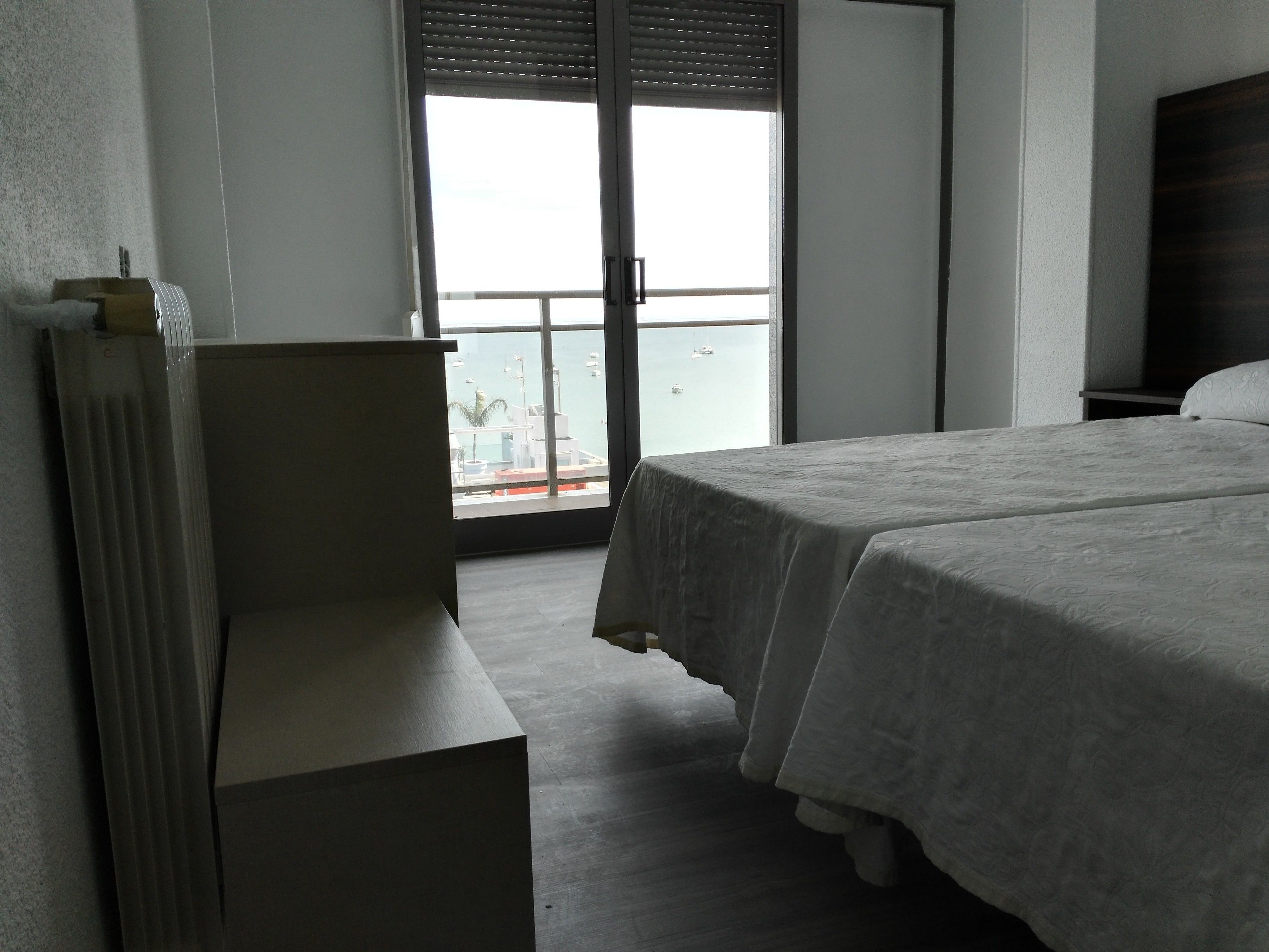 Habitación de hotel con cama, escritorio y vista al mar a través de un amplio ventanal.