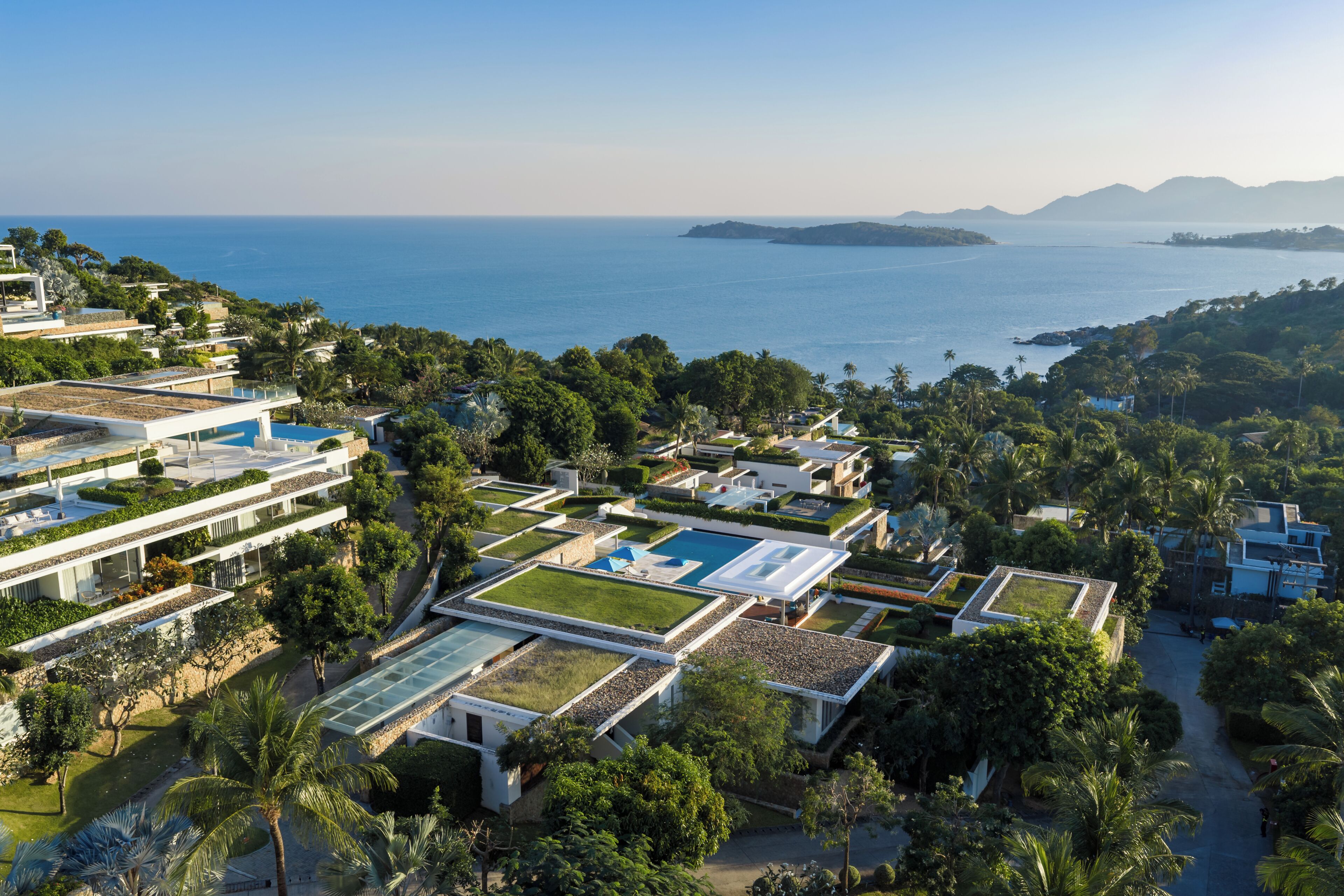 Ein modernes Resort mit mehreren Gebäuden, einem zentralen Poolbereich und Blick auf das Meer.