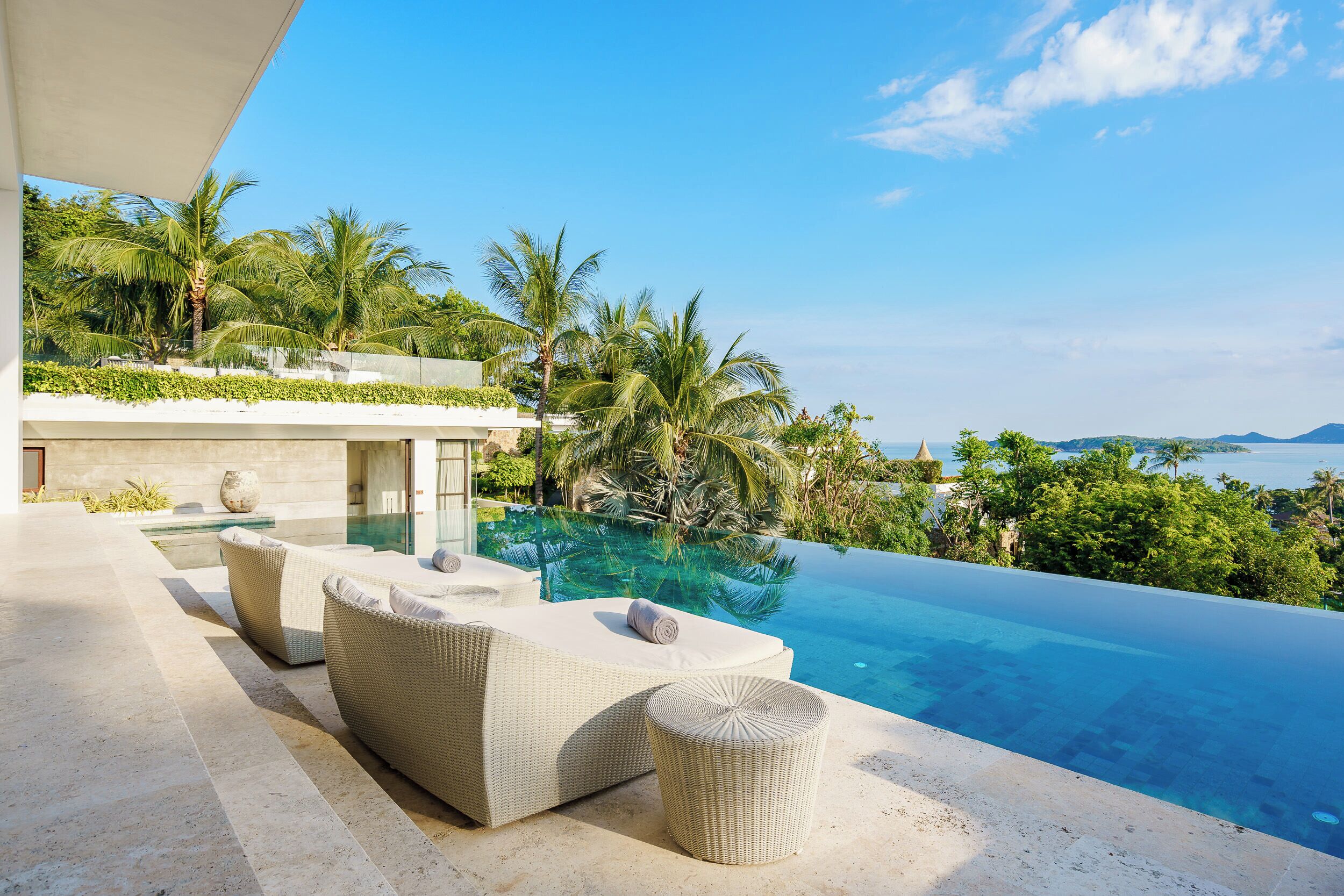 An infinity pool with wicker furniture and a view of the ocean.