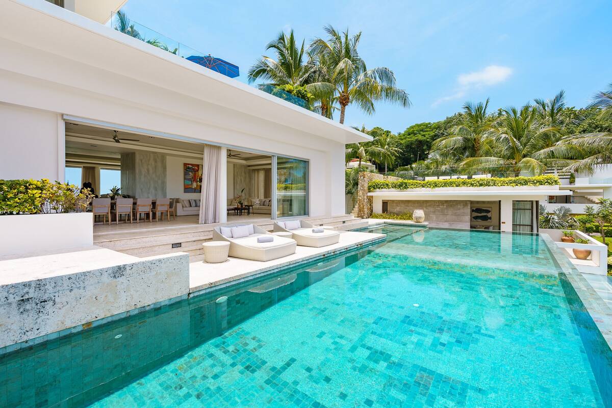 A modern house with a swimming pool, outdoor seating, and a view of palm trees.
