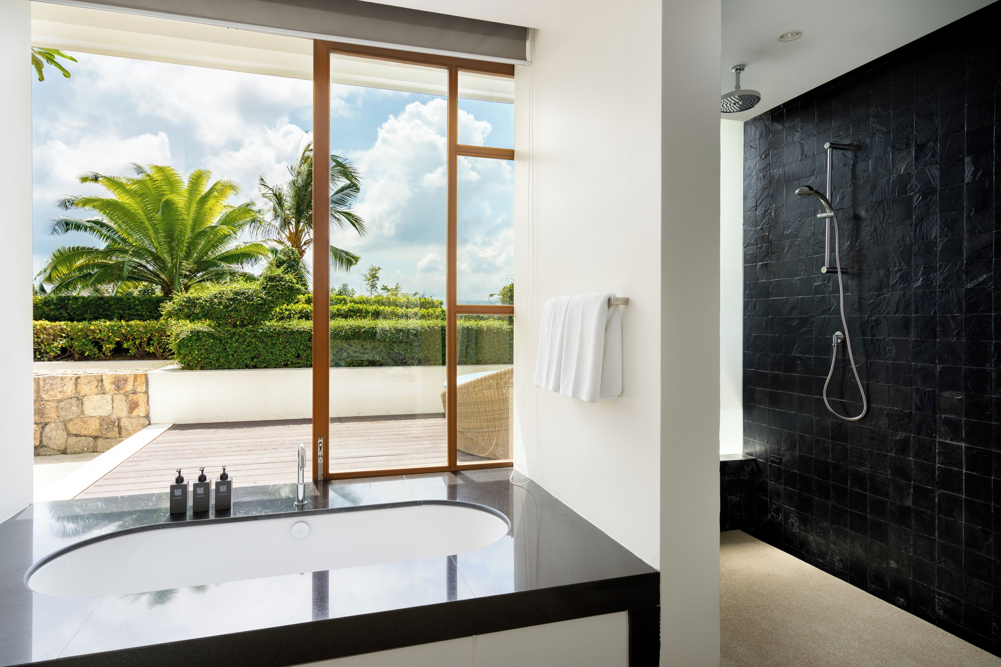 A modern bathroom with a large bathtub, a shower, and a view of a landscaped garden.