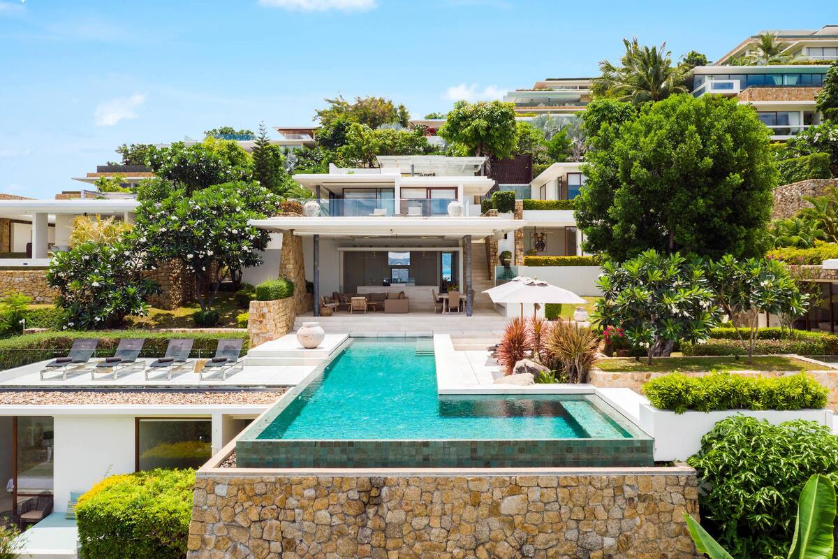 A modern house with a swimming pool, outdoor furniture, and lush landscaping.