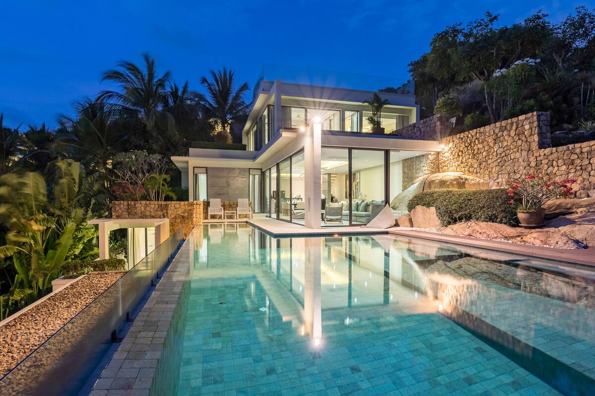 Uma casa moderna com piscina, muro de pedra e plantas tropicais.