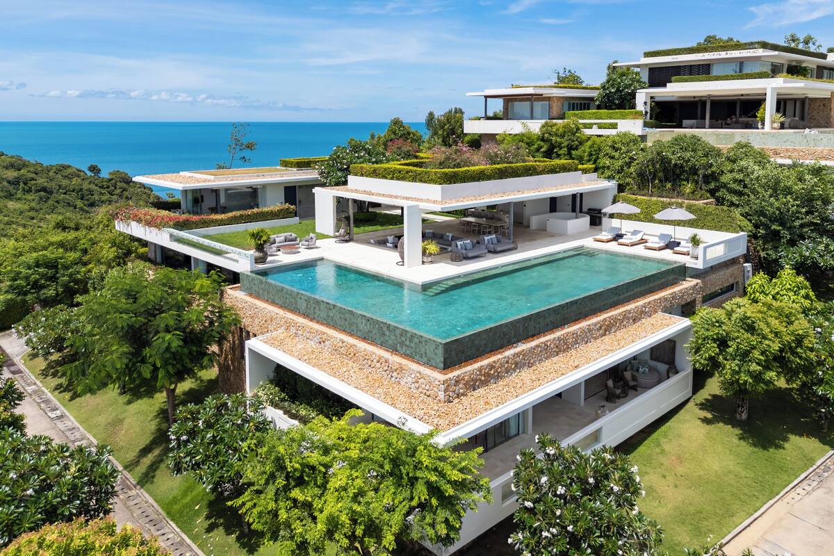 A luxurious property with a large swimming pool, multiple modern houses, and a scenic ocean view.