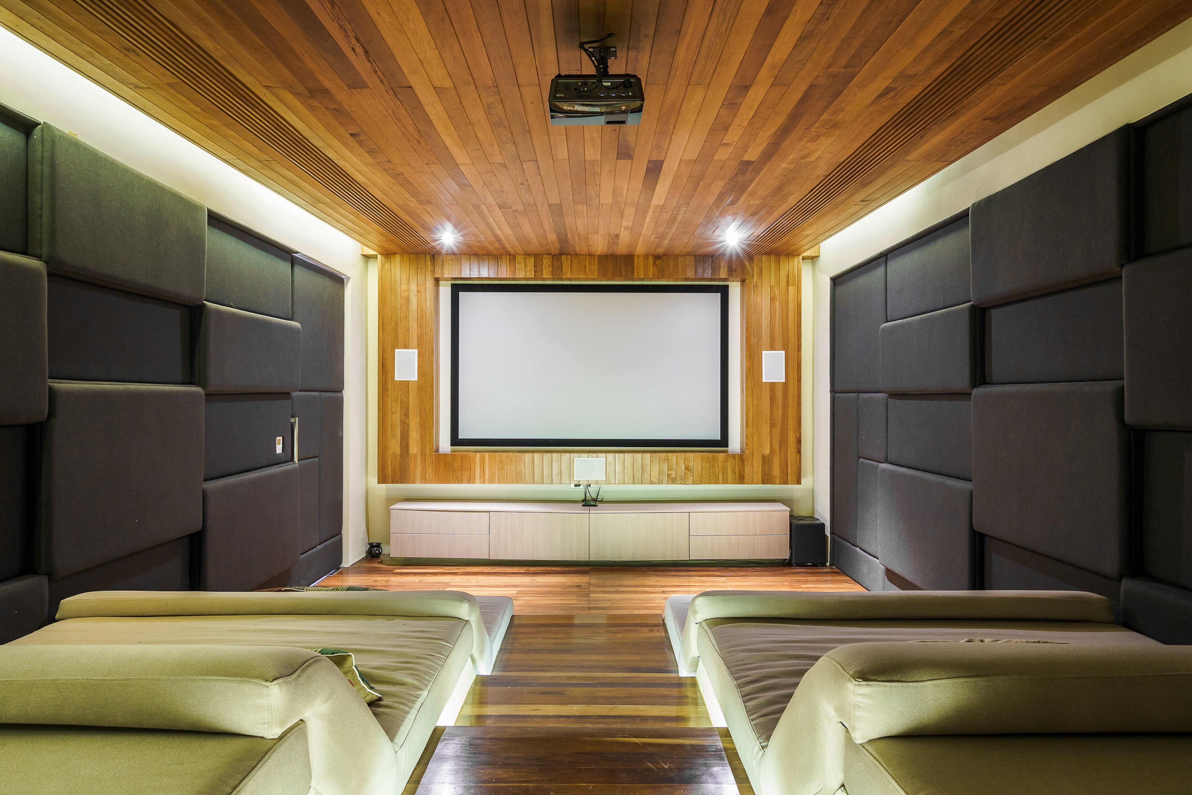 Une salle de cinéma privée dotée d’un grand écran, d’un plafond en bois et de sièges rembourrés.