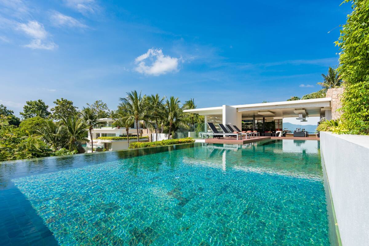 A clear blue infinity pool with lounge chairs and a modern building in the background.