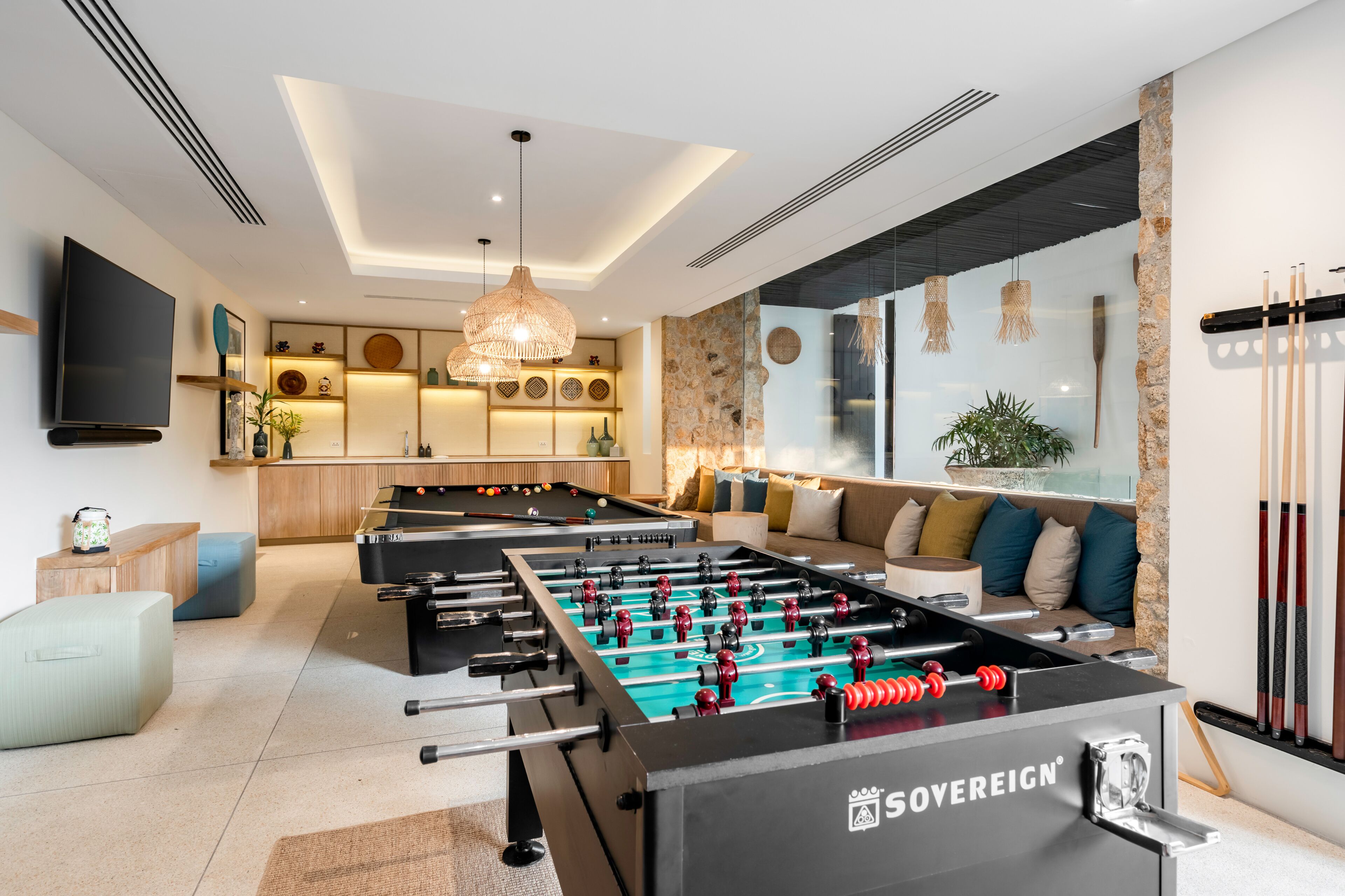 A modern living room with a foosball table, a flat-screen TV, and a cozy seating area with cushions.