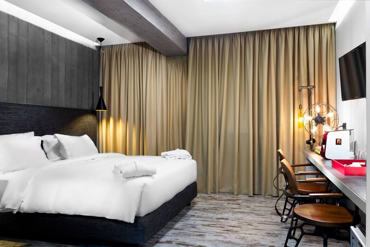 A hotel room with a bed, a desk with a chair, a TV, and curtains.