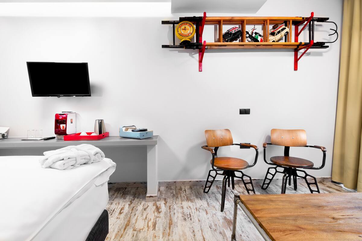 A hotel room with a bed, a desk, a television, two chairs, and a shelf with toys.
