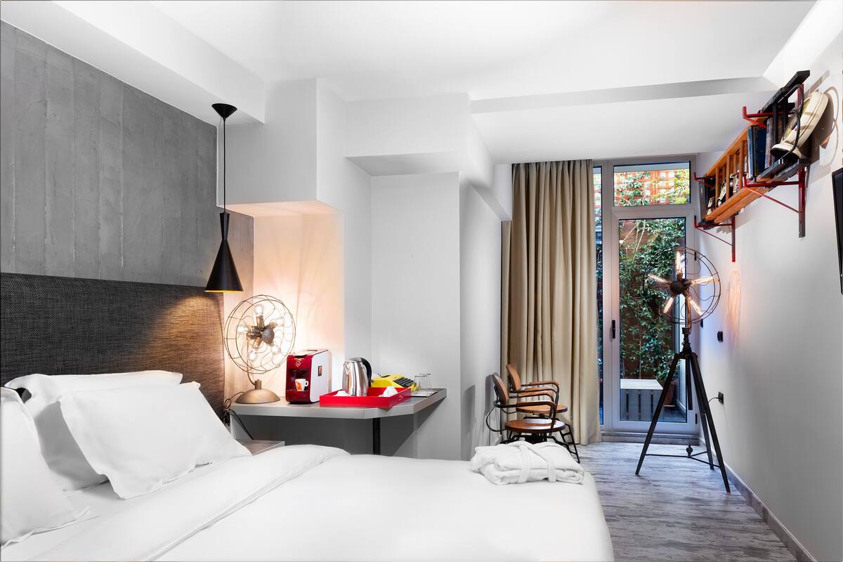 A hotel room with a bed, bedside table, lamp, chair, and a view of the outdoors.