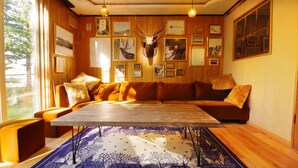 A cozy room with a wooden ceiling, a mounted deer head, a wooden table, and a patterned rug. - Shiretoko Village (Shari)