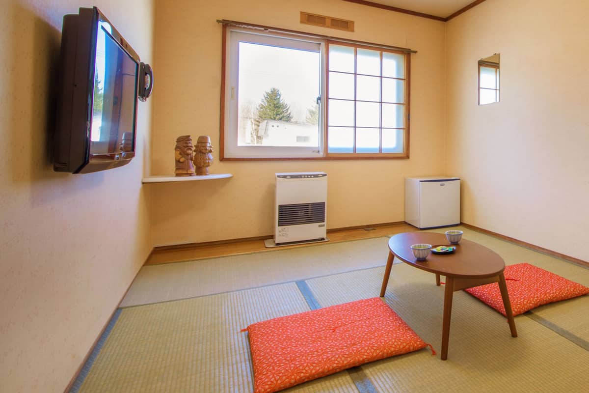 A room with tatami mats, a low table with a cushion, a television, and a window with a view of a tree.