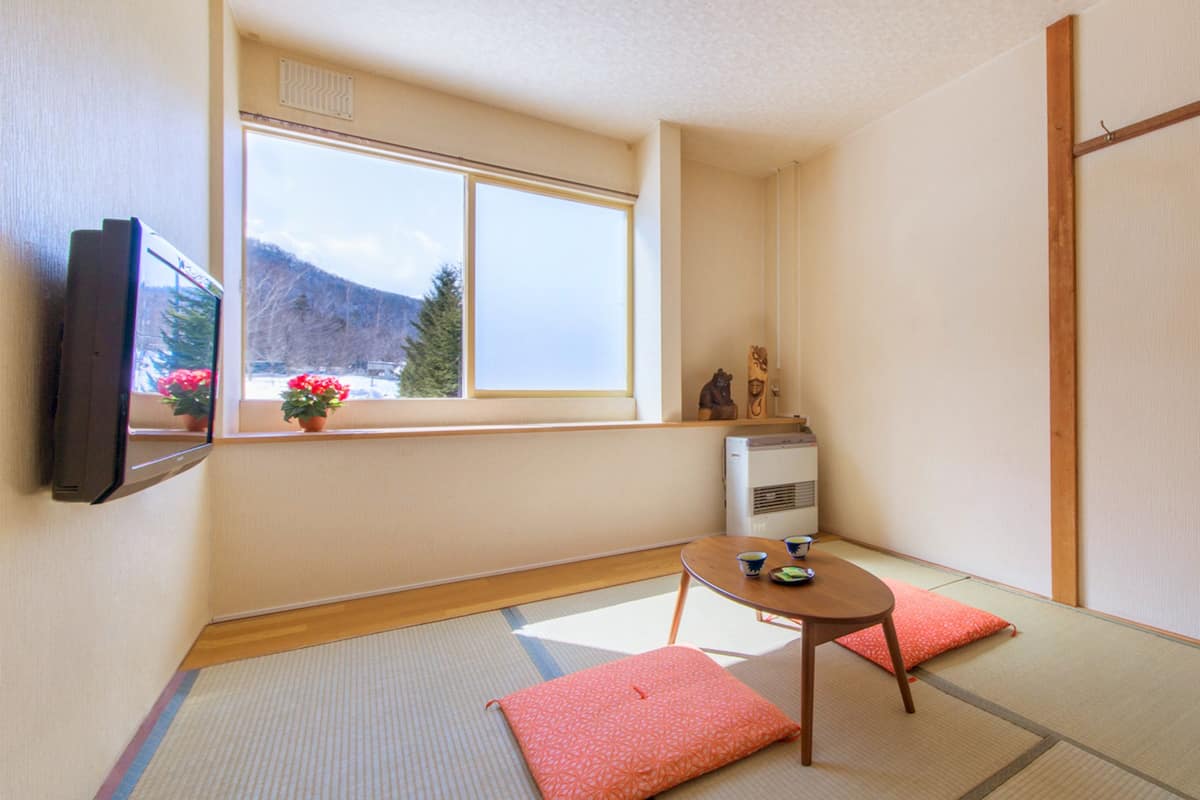 A traditional Japanese room with tatami flooring, a sliding door, a small table with a cup, and a TV on the wall.