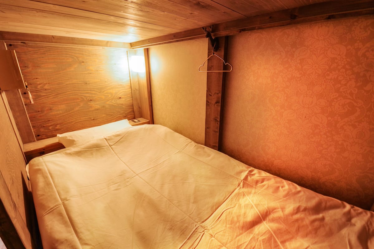 A small, single-bed room with wooden walls and a simple bed.