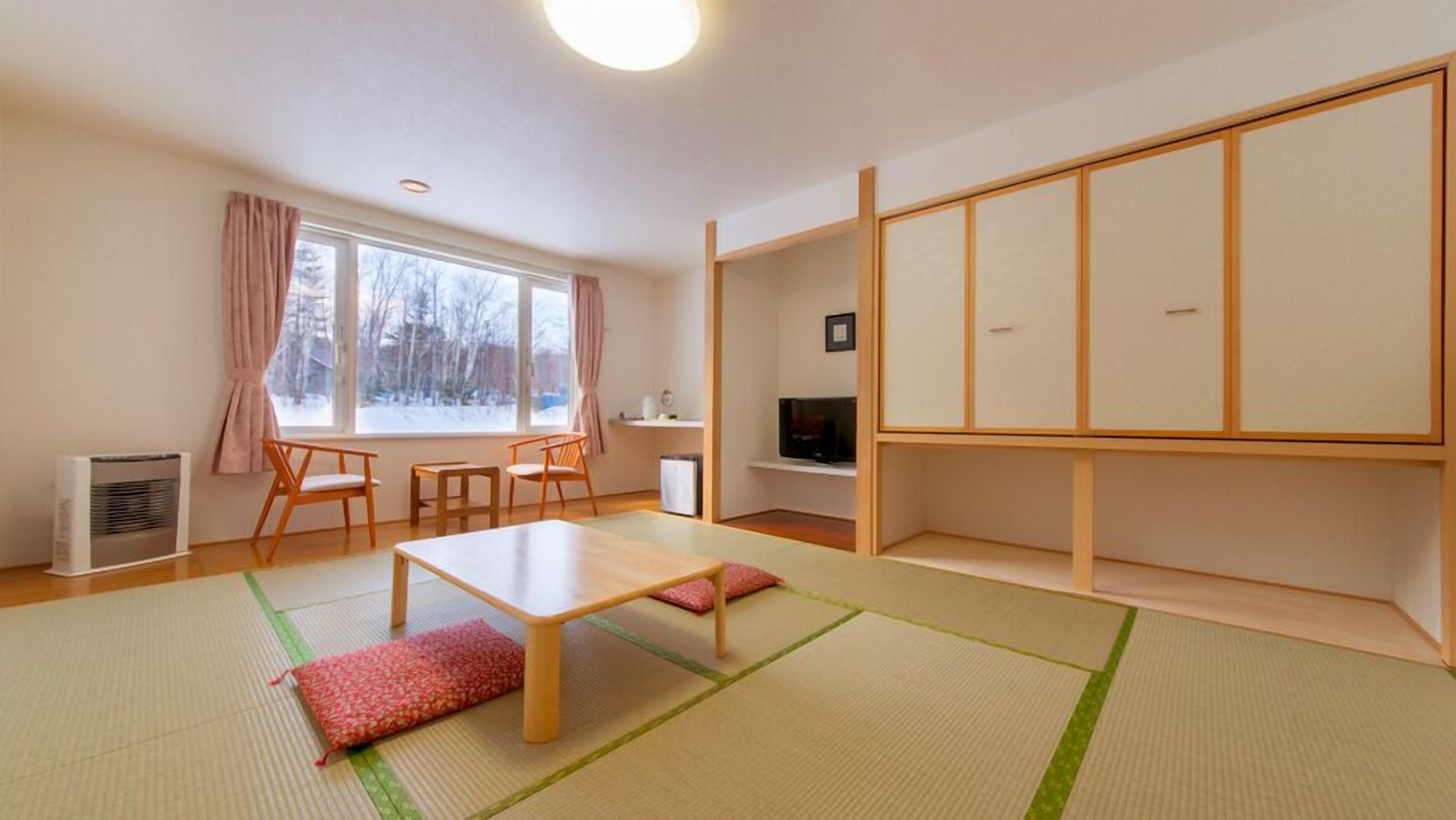 Ein Zimmer mit Tatami-Böden, einem niedrigen Tisch, Stühlen, einem Fernseher und einer großen Schiebetür.