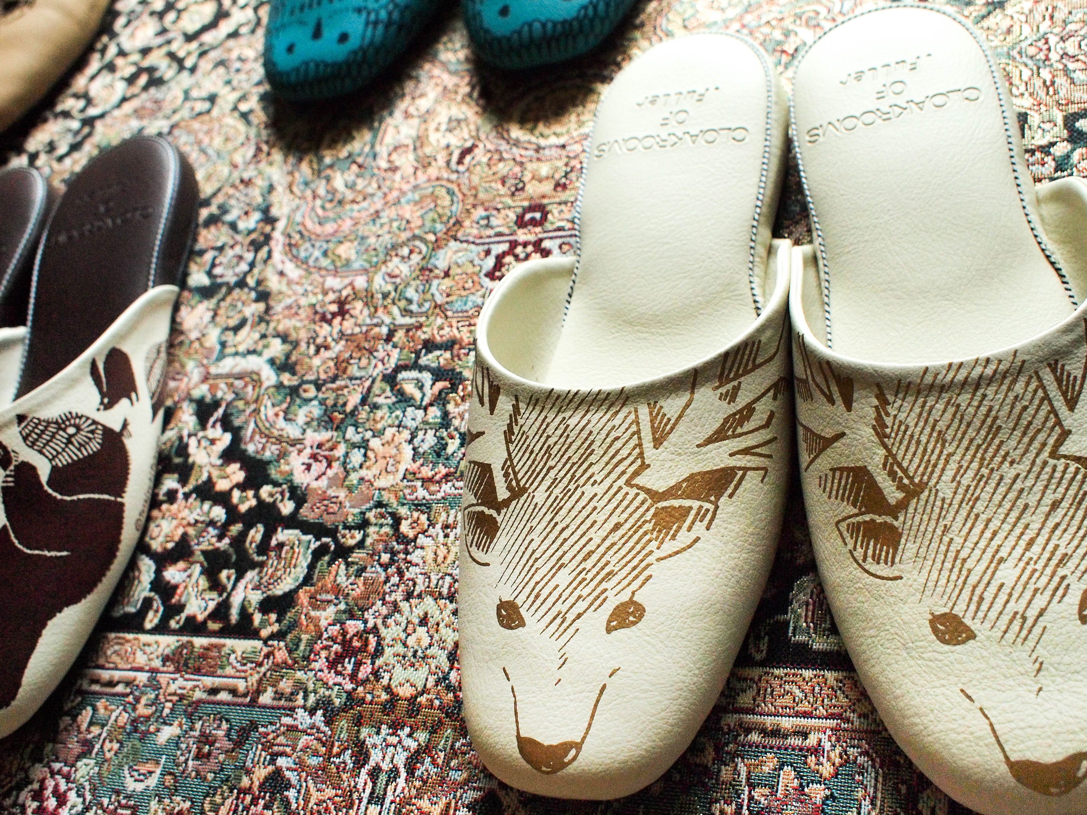 Un par de pantuflas blancas con diseño animalado en tonos marrones, sobre una alfombra estampada.