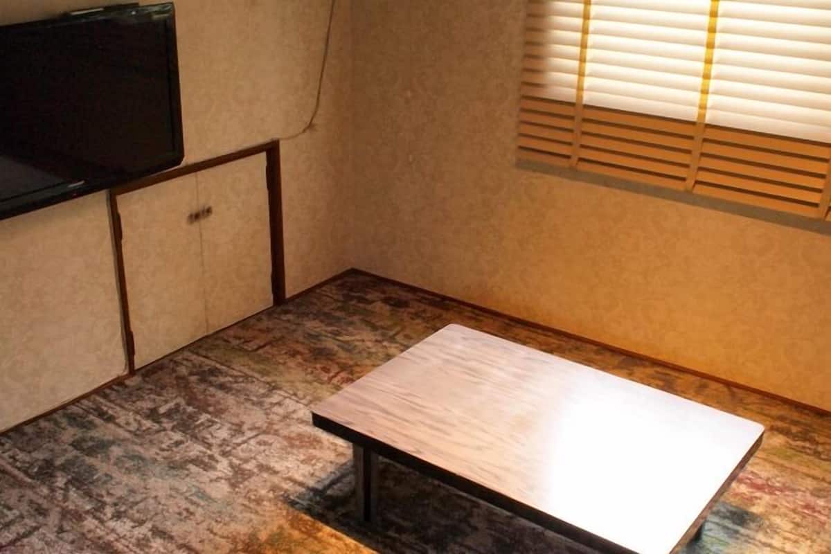 A small room with a television mounted on the wall, a wooden table, and a window with blinds.
