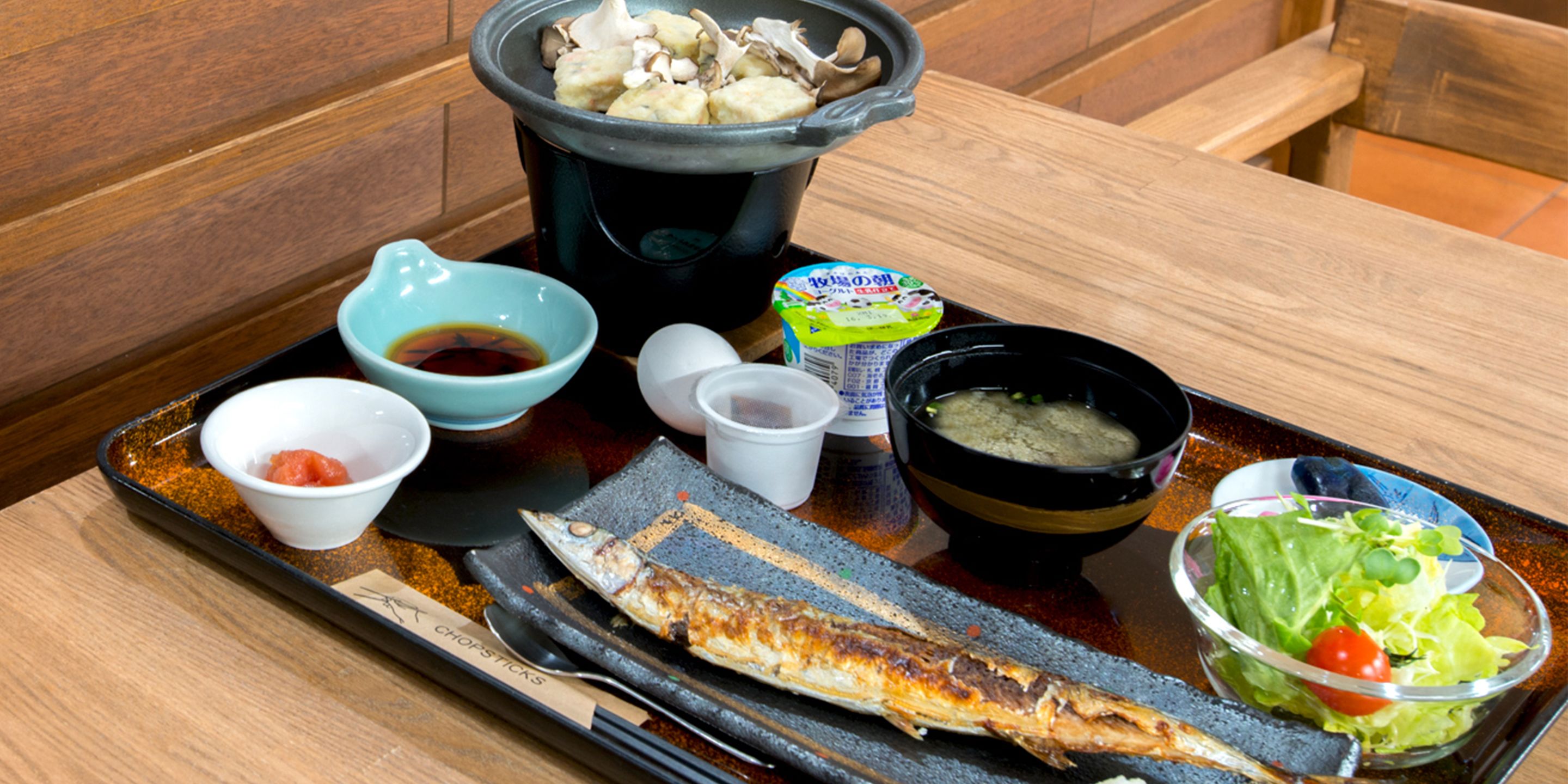 A tray with grilled fish, a bowl of soup, a bowl of salad, and a pot of mushrooms.