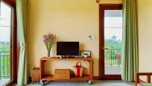 Una habitación con una televisión sobre un mueble de madera, una mesita con un florero, una cesta y una alfombra roja.