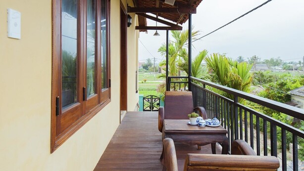 Un balcón de madera con una mesa y sillas, con vistas a un jardín y edificios lejanos.