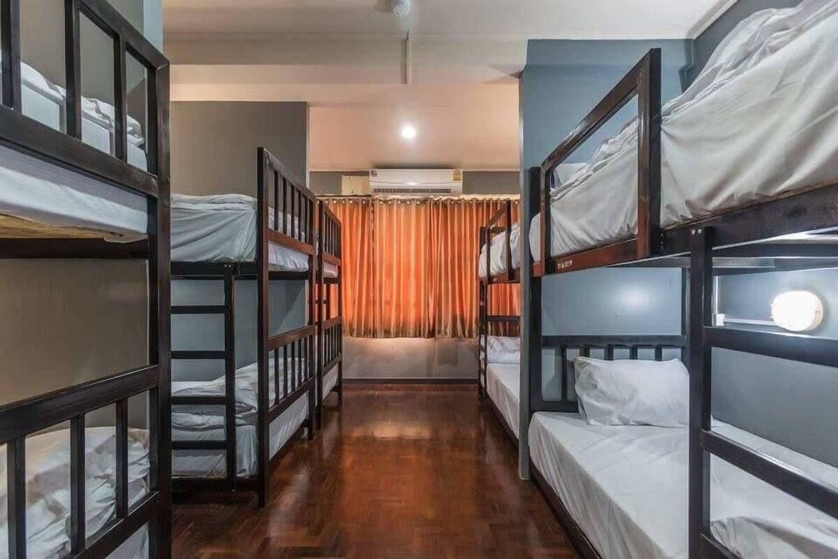 A room with bunk beds arranged in two rows, wooden flooring, and an air conditioning unit on the wall.